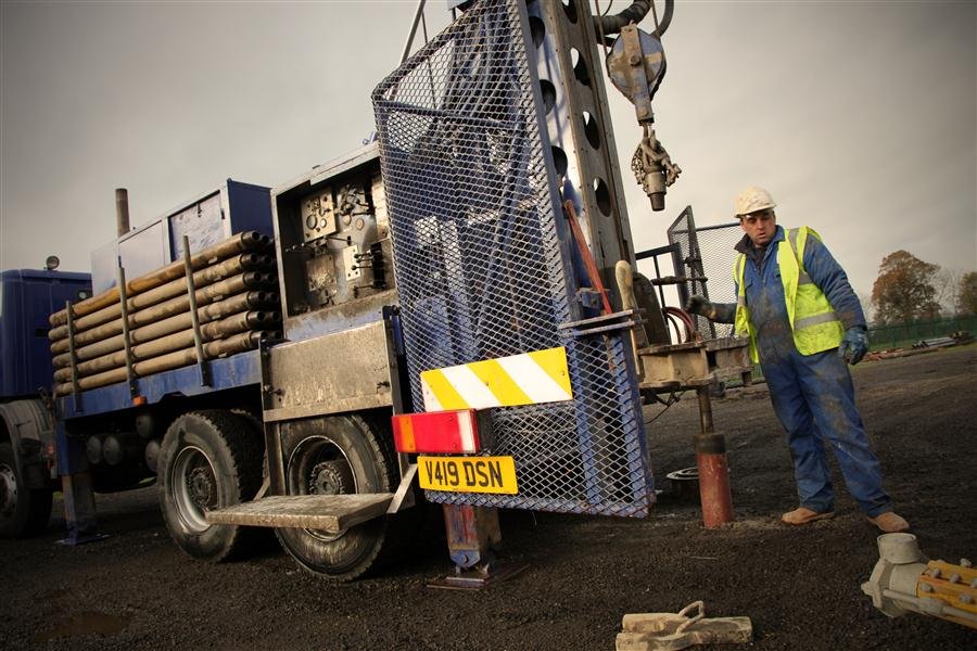 Drilling crew member beside a rotary rig with drill pipe during a well installation